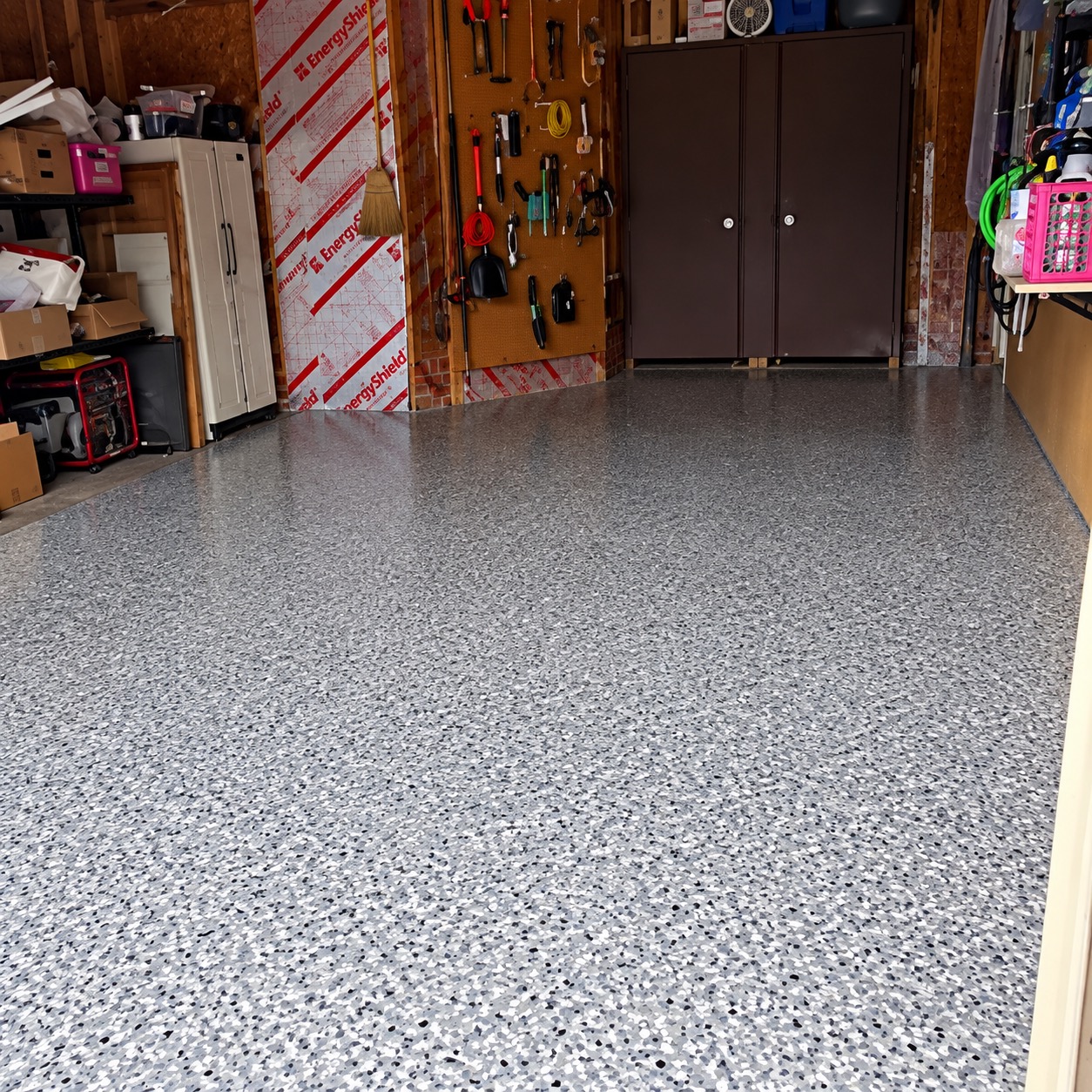 The same garage after coating: an even gray, white and black flake floor in front of the brown storage cabinets