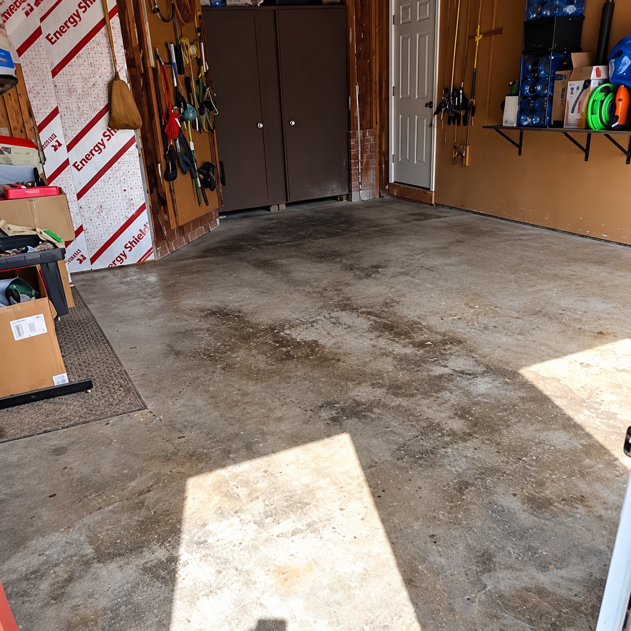 Garage floor before coating: bare concrete with dark oil and water stains in front of brown storage cabinets