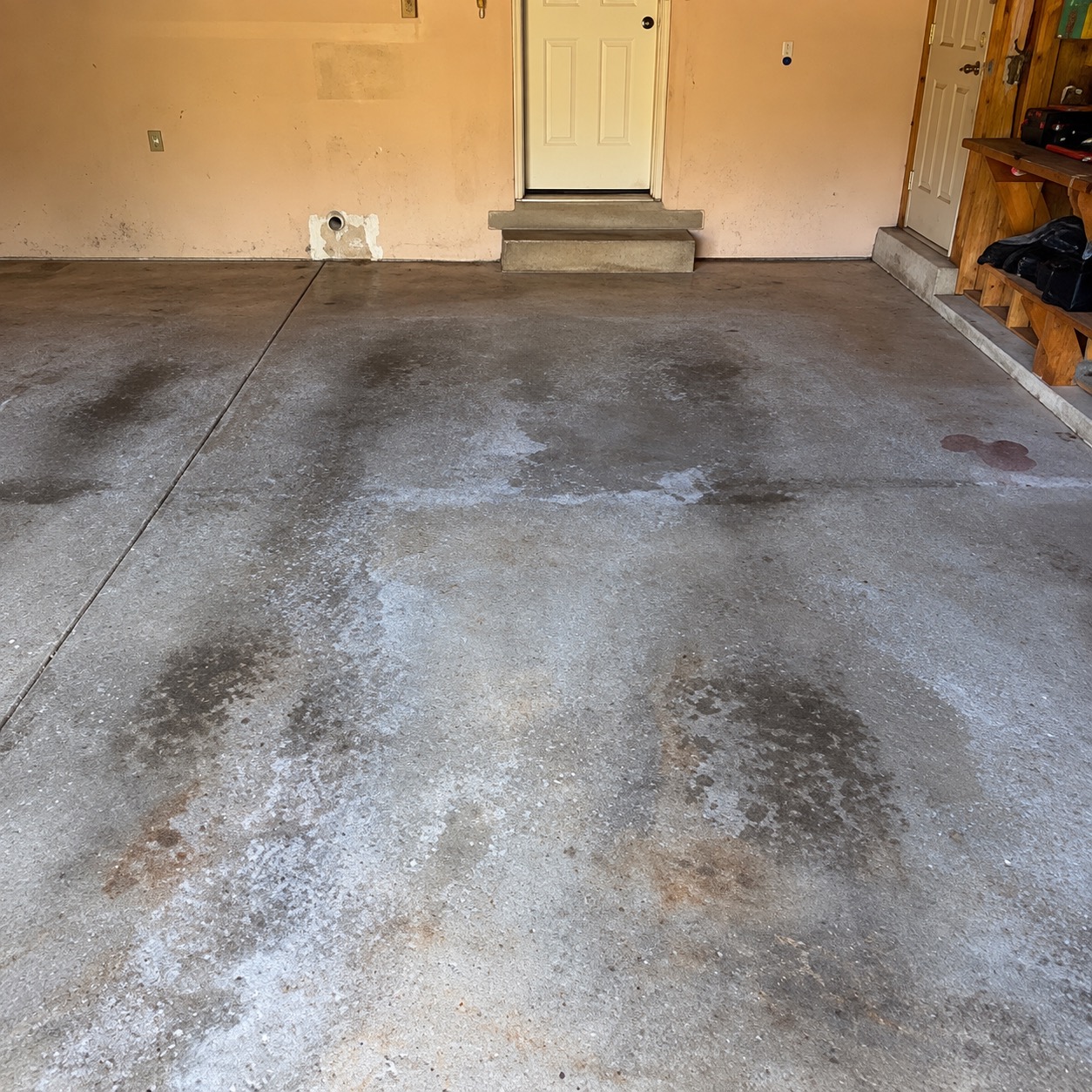Garage before coating: bare concrete with oil stains, tire tracks, white salt residue and rust spots in front of the house door step
