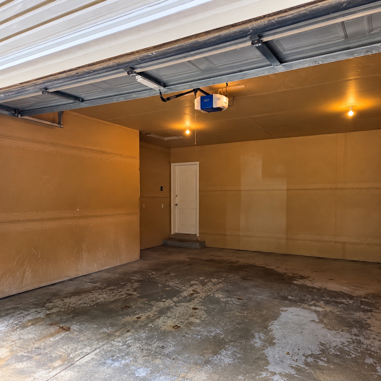 Garage before coating: bare concrete with water marks and stains, tan walls, and an uncoated step at the house door