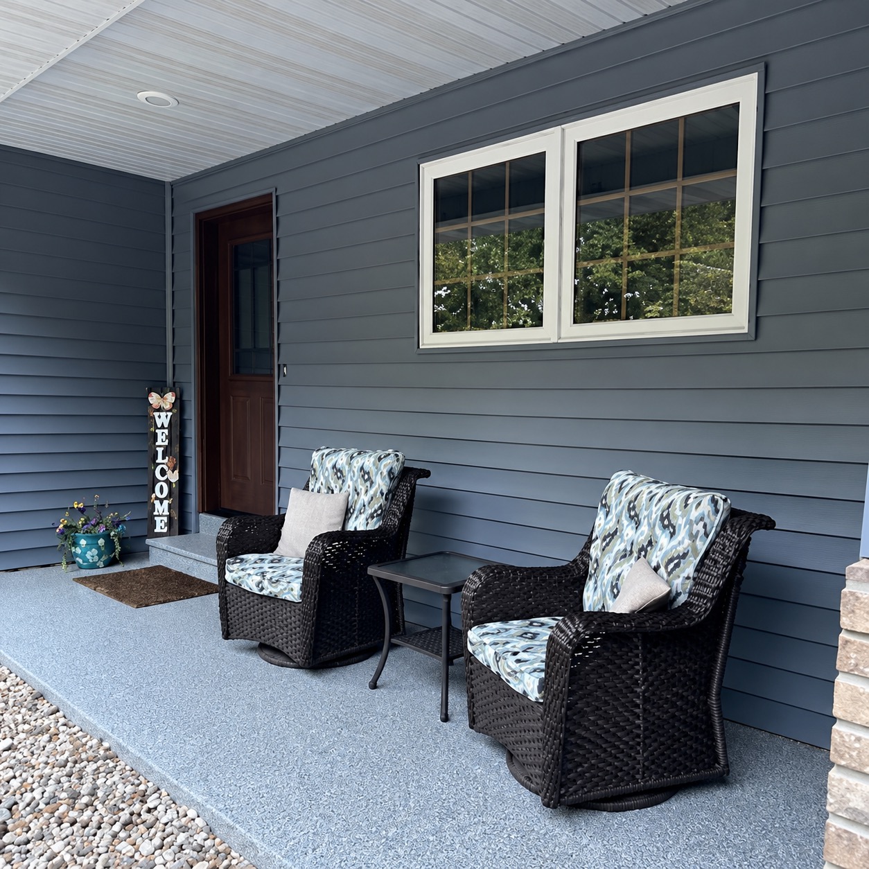 Covered front porch with a light gray flake coating on the slab and entry step, wicker chairs against blue siding