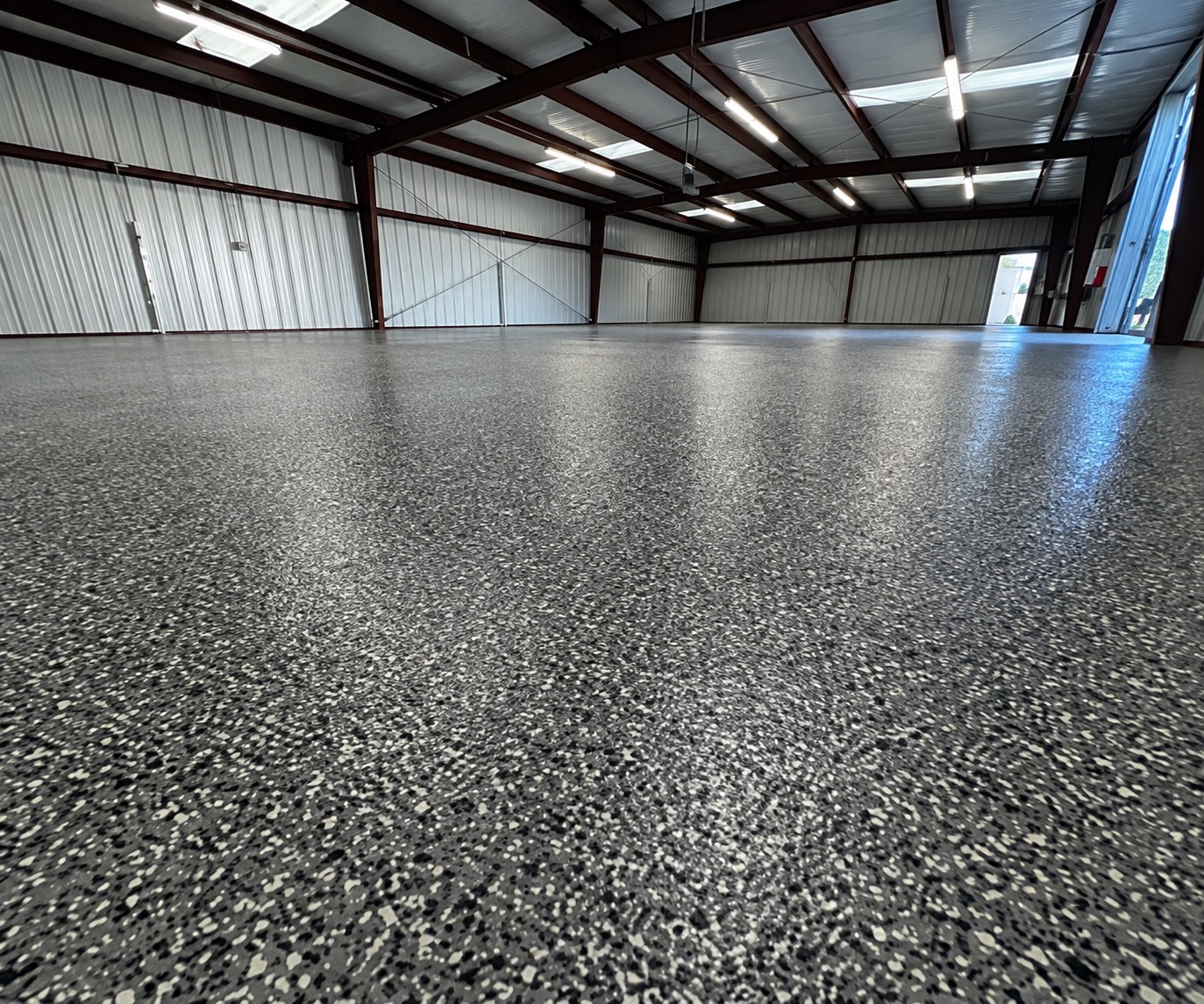 Low-angle view of a glossy gray, black and white flake floor across a large steel-frame commercial building